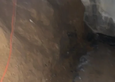 Blurry image of an underground excavation site with exposed earth and a power cord running along the ground. Natural light from a window above